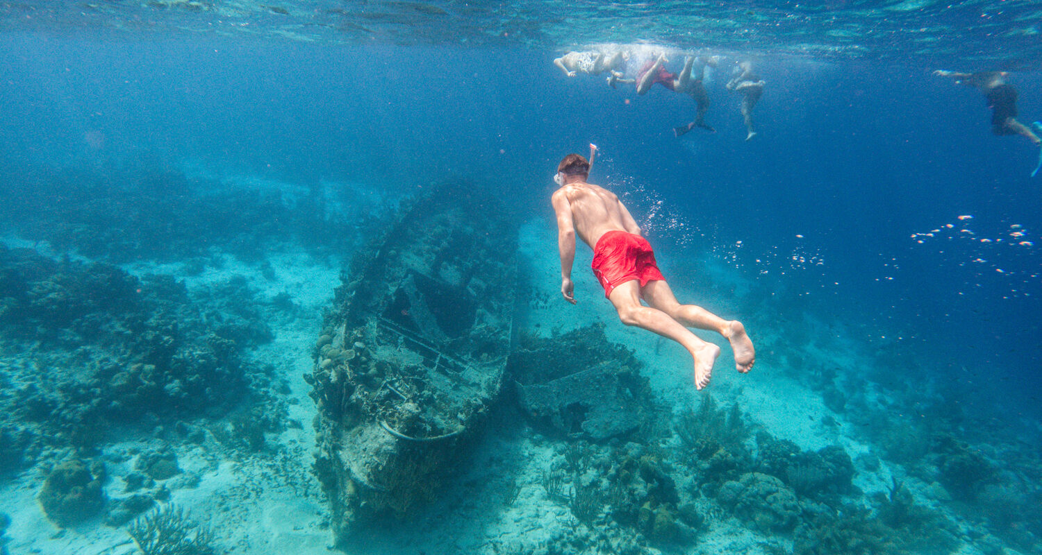 guy with red swim shorts snorkeling towards ship wreck