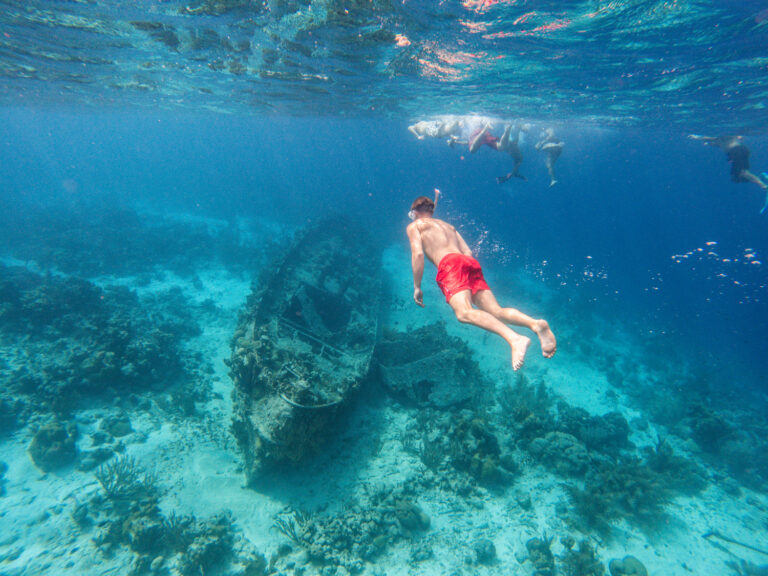 guy with red swim shorts snorkeling towards ship wreck